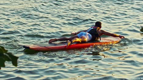Man-lying-on-paddle-board,-swimming-during-golden-hour-in-slow-motion