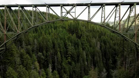 flying-below-of-a-bridge-and-on-top-of-a-forest,-The-High-Steel-Bridge-is-a-truss-arch-bridge-that-spans-the-south-fork-of-the-Skokomish-River-in-Mason-County,-Washington