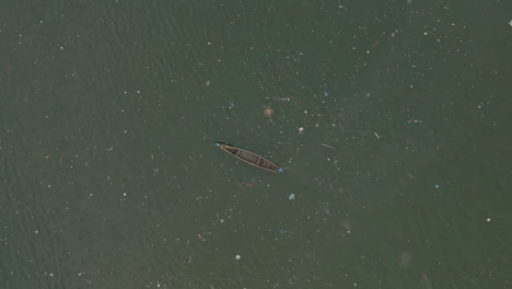 Aerial-footage-following-a-canoe-moving-through-trash-in-the-water