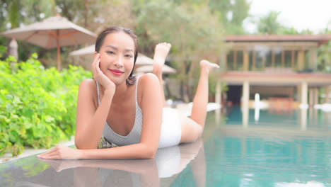 Happy-Smiling-Exotic-Female-Model-in-Swimsuit-Lying-on-Pool-Edge,-Holding-Head-and-Looking-at-Camera,-Slow-Motion