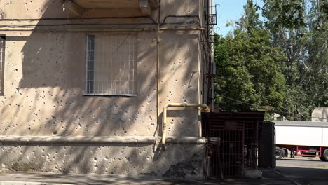 Traffic-passes-the-wall-of-a-residential-housing-block-that-is-riddled-with-shrapnel-holes-following-a-Russian-missile-strike-a-day-earlier-that-destroyed-the-rear-buildings