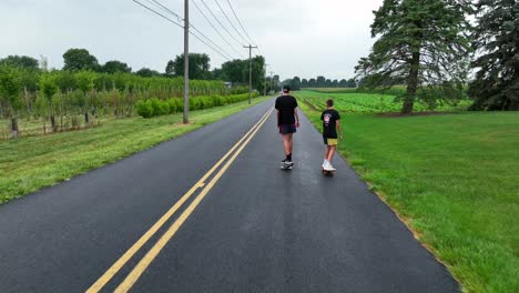 Two-teenage-boys-riding-skateboards-on-rural-street-in-America