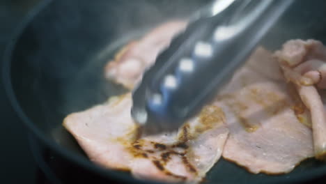 Raw-ham-slices-cooking-in-a-black-pan