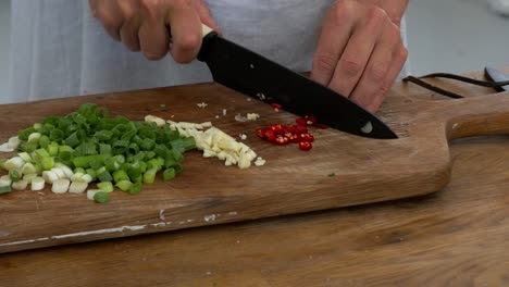 Slicing-fresh-hot-chillies-on-a-board-among-celery-and-garlic-in-preparation-to-cook