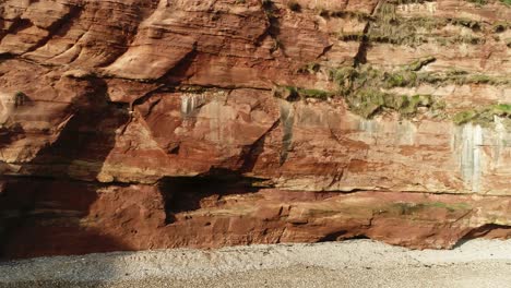 Aerial-tracking-shot-of-red-sandstone-cliff-on-the-Jurassic-coast