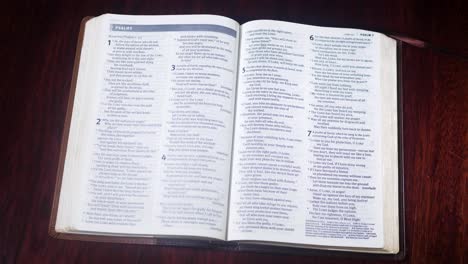 Abriendo-Una-Biblia-Marrón-Al-Libro-De-Salmos-En-Un-Escritorio-De-Mesa-Marrón