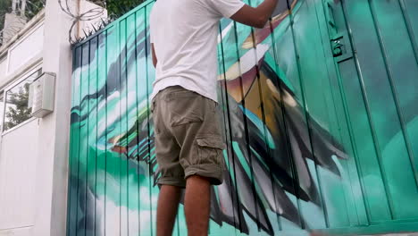 Graffiti-artist-is-spray-painting-a-tropical-bird-on-a-metal-gate