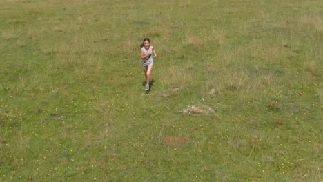 Young-girl-run-in-green-field---aerial-tracking-shot