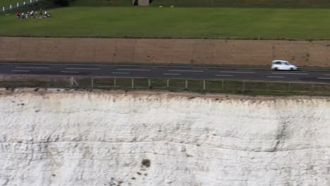 Aerial-profile-shot-of-holiday-makers-using-the-A259-coast-road-near-Brighton,-UK-above-chalk-cliffs
