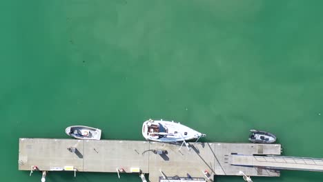 Top-down-aerial-view-of-a-man-mooring-a-sailing-boat-on-the-turquoise-waters-of-Brighton-Marina,-UK
