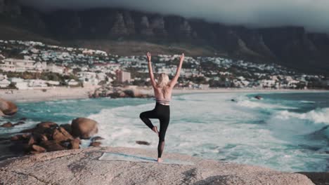 Schöne-Und-Gesunde-Frau,-Die-Eine-Yoga-Pose-Vor-Einer-Atemberaubenden-Blauen-Meereslandschaft-Mit-Nebligen-Bergen-Im-Hintergrund-Macht
