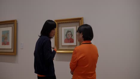 Frauen-Gestikulieren-–-Diskussion-In-Der-Taiwanesischen-Kunstgalerie-über-Zeitgenössische-Kunst-An-Der-Wand