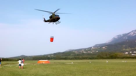 Helicóptero-Con-Balde-Tomando-Agua-Para-Combatir-Un-Incendio-Forestal,-Bomberos-Con-Camiones-Brindan-Apoyo-En-Tierra