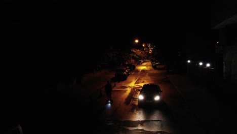 Luftaufnahme-Eines-Nachts-Ausweichenden-Autos,-Das-An-Einem-Fußgänger-Auf-Einem-Staubsaugerbrett-Vorbeifährt