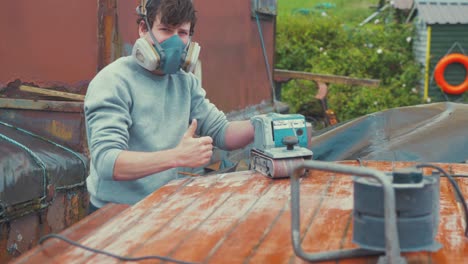Young-man-thumbs-up-satisfied-with-sanding-job-boat-roof