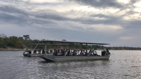 Two-photo-safari-tour-boats-with-guests-pass-on-Chobe-River,-Africa