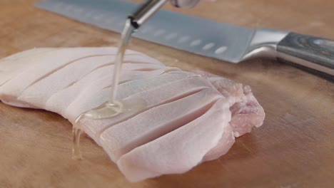 Close-Interior-Slider-Shot-in-Slow-Motion-of-Olive-Oil-Drizzling-on-a-Piece-of-Belly-Pork-on-a-Wooden-Chopping-Board-Next-to-a-Chef-Knife