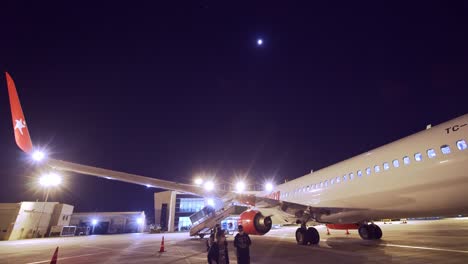 People-Wearing-face-masks-for-corona-Walking-outside-plane-at-night-at-Kayseri-Erkilet-Airport-In-Turkey-With-An-Airplane-Of-Corendon-Airline-Parked-in-the-dark---covid-virus-pandemic-lockdown-flying