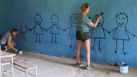 Young-woman-paints-children-figures-inside-school's-classroom-wall