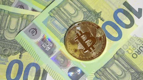 Männliche-Hand-Legt-Hundert-Euro-Banknote-Und-Einen-Einzelnen-Goldenen-Bitcoin-Auf-Einen-Stapel-Hundert-Euro-Banknoten