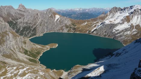 Eine-Drohnenaufnahme-Des-Heart-Love-Lake-In-Der-Schweiz-Bewegt-Sich-Rückwärts-Und-Zeigt-Einen-Jungen-Mann,-Der-Stark-Und-Stolz-Auf-Einer-Klippe-Steht-Und-Auf-Die-Atemberaubende-Landschaft-Vor-Sich-Blickt