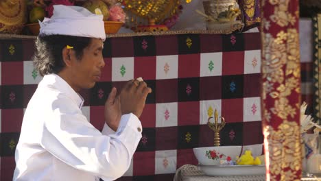 Priest-prays-with-folded-hands-and-eyes-closed-at-outdoor-altar-in-Ubud,-Bali,-Indonesia
