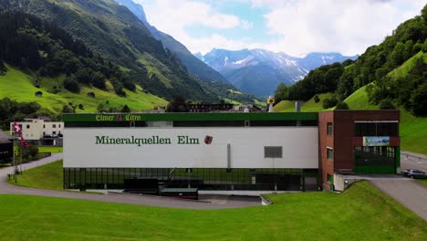 Rising-aerial-cinematic-shot-of-Elmer-mineral-water-plant-in-Elm,-Glarus,-Switzerland