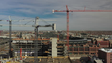 Rising-aerial-drone-footage-of-multiple-construction-cranes-with-Coors-field-in-the-background,-in-Denver,-Colorado