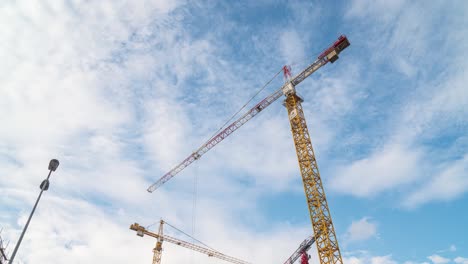 Timelapse-of-cranes-on-construction-site,-blue-sky-with-moving-clouds,-low-angle-static-view