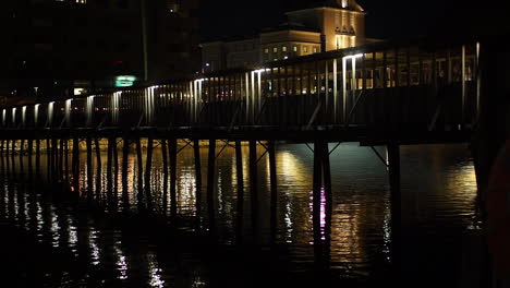 Illuminated-pedestrian-bridge-over-a-river-in-the-city-at-night