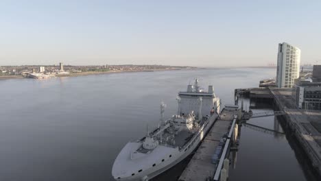 Liverpool-waterfront-aerial-view-royal-navy-military-ship-sunrise-high-rise-buildings-skyline-pull-back