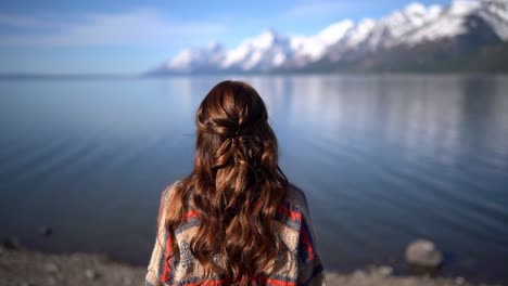 Amazing-view-a-young-attractive-brunette-girl-standing-in-front-of-the-water-looking-in-the-distance-with-the-backdrop-of-a-lake