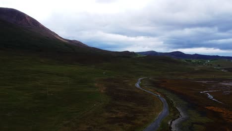 Tilt-down-drone-shot-of-car-driving-by-on-highland-road-landscape