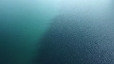 Drone-flight-over-a-brilliant-blue-lake-with-different-shades-of-blue-and-wind-that-creates-waves-on-the-surface-of-the-water