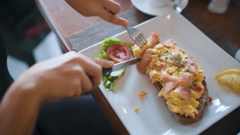 Female-cutting-and-eating-a-sandwich-with-salmon-and-eggs-on-toasted-bread