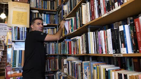 A-man-is-looking-for-books-in-a-bookstore-or-library,-interior-with-bookshelves
