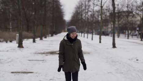 Girl-in-park-in-winter-reaching-down-to-pick-up-snow-from-ground,-slow-motion