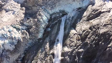 Vista-Aérea-De-Una-Cascada-Con-Agua-Derretida-De-Un-Glaciar-Moribundo-En-Suiza