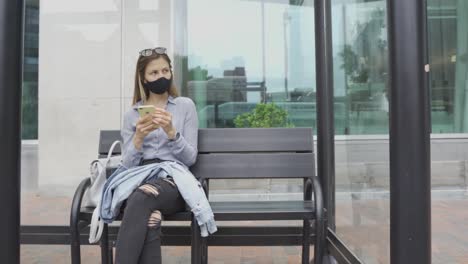 Junges-Mädchen-Mit-Gesichtsmaske-Sitzt-An-Einer-Bushaltestelle-Und-Wartet-Auf-öffentliche-Verkehrsmittel