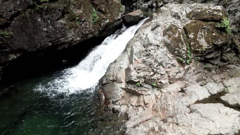 Fresh-clear-water-cascades-over-a-boulder-strewn-mountain-creek,-aerial-reveal