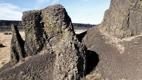 Flying-through-ancient-basalt-columns-to-reveal-the-bleak-desert-canyon-below,-aerial