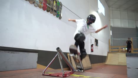 Low-angle-slow-motion-of-young-boy-with-mask-jumping-with-skateboard-over-ramp-and-rail
