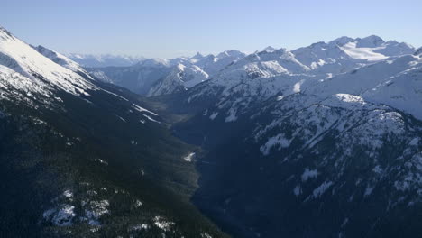 Beautiful-aerial-view-of-snow-covered-mountains-peaks-and-overgrown-valley-during-sunny-day-in-winter