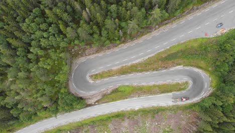 Tractor-driving-down-winding-mountain-forest-road-hairpins,-aerial-top-down-view