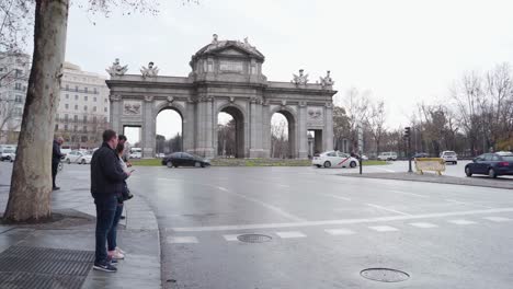 Gente-Esperando-Para-Cruzar-La-Calle-Con-Vehículos-Circulando-Por-La-Carretera-Cerca-De-La-Puerta-De-Alcalá-En-La-Plaza-De-La-Independencia,-Madrid,-España