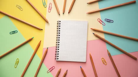 Stop-motion-of-a-notebook,-colorful-paper-clips-and-wooden-pencils-on-pastel-colored-paper