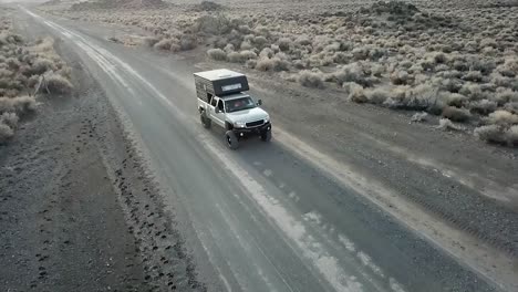 Truck-driving-on-a-dirt-road-in-the-desert,-aerial-wide-tracking-shot