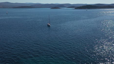 Aerial-View-of-Lighthouse-Tower-on-Small-Island-and-Sailing-Boat-in-Blue-Sea-on-Sunny-Day-With-Croatian-Coastline-in-Background,-50fps-Drone-Shot
