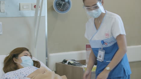 Female-Nurse-With-Face-Mask-Assisting-A-Middle-Aged-Female-Patient-To-Sit-Down