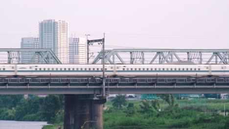 Un-Tren-Bala-Shinkansen-Modelo-N700-Que-Pasa-Sobre-Un-Puente-En-El-Río-Tamagawa-Con-Rascacielos-Al-Fondo-En-Tokio,-Japón---Toma-De-Trípode